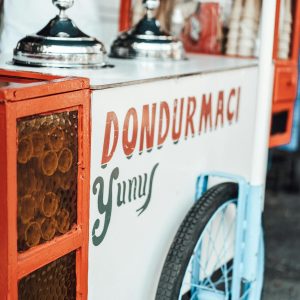 Food cart with metal lids and various ingredients with colorful inscription parked on asphalt sidewalk on street in city on blurred background