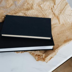 From above of notebook pair with black empty hardcover placed with packing paper and white marble table during prepare for postal delivery